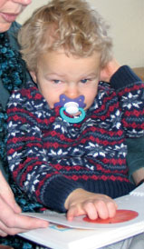 Blind toddler reading a Braille and large print book with his mother. The colorful pictures of simple objects are sculpted and embossed so that he can feel them all in Sadie Can Count by Ann Cunningham. 